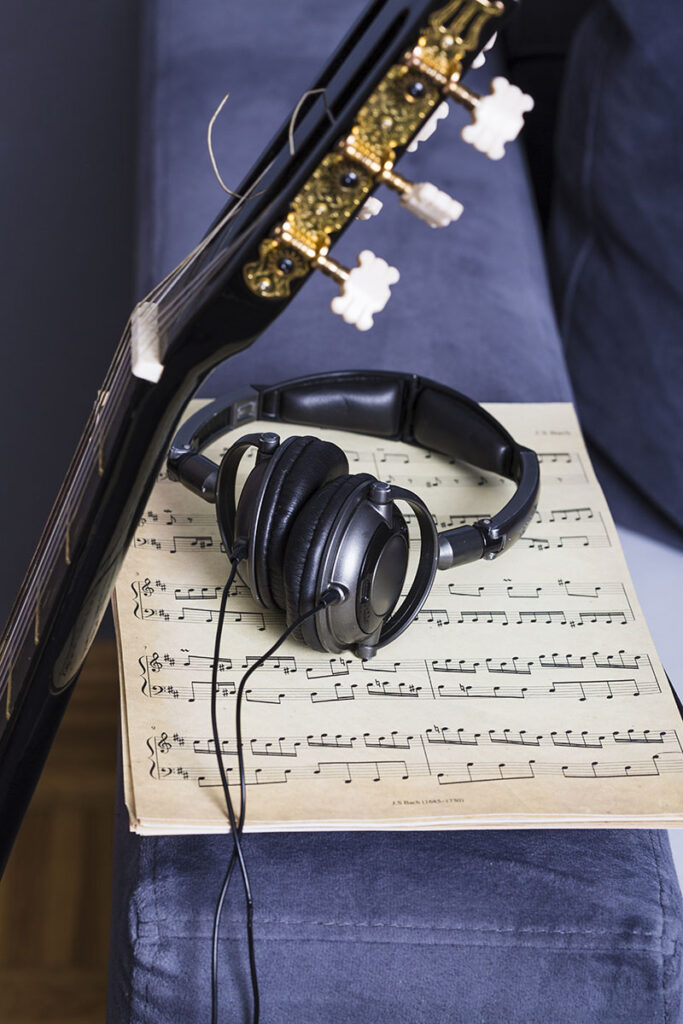 Imagem com uma partitura, um violão e um fone de ouvido